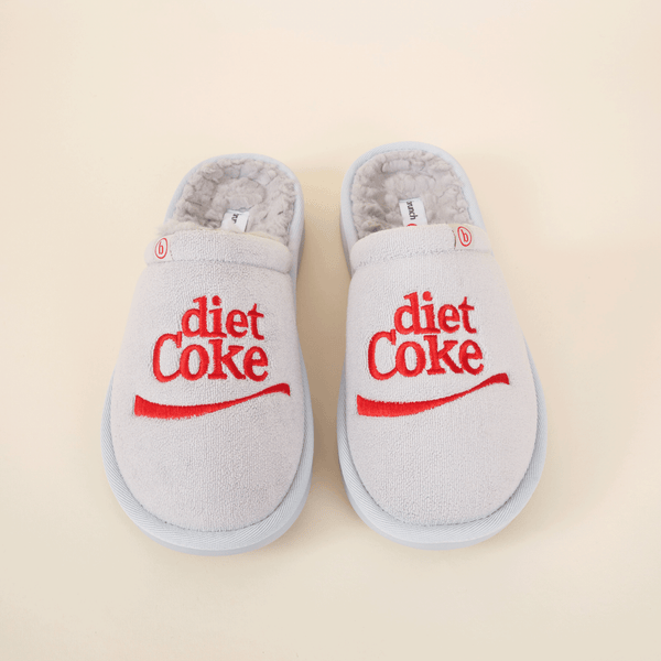 Top-down view of grey shearling slippers with red embroidered diet Coke logo on beige background