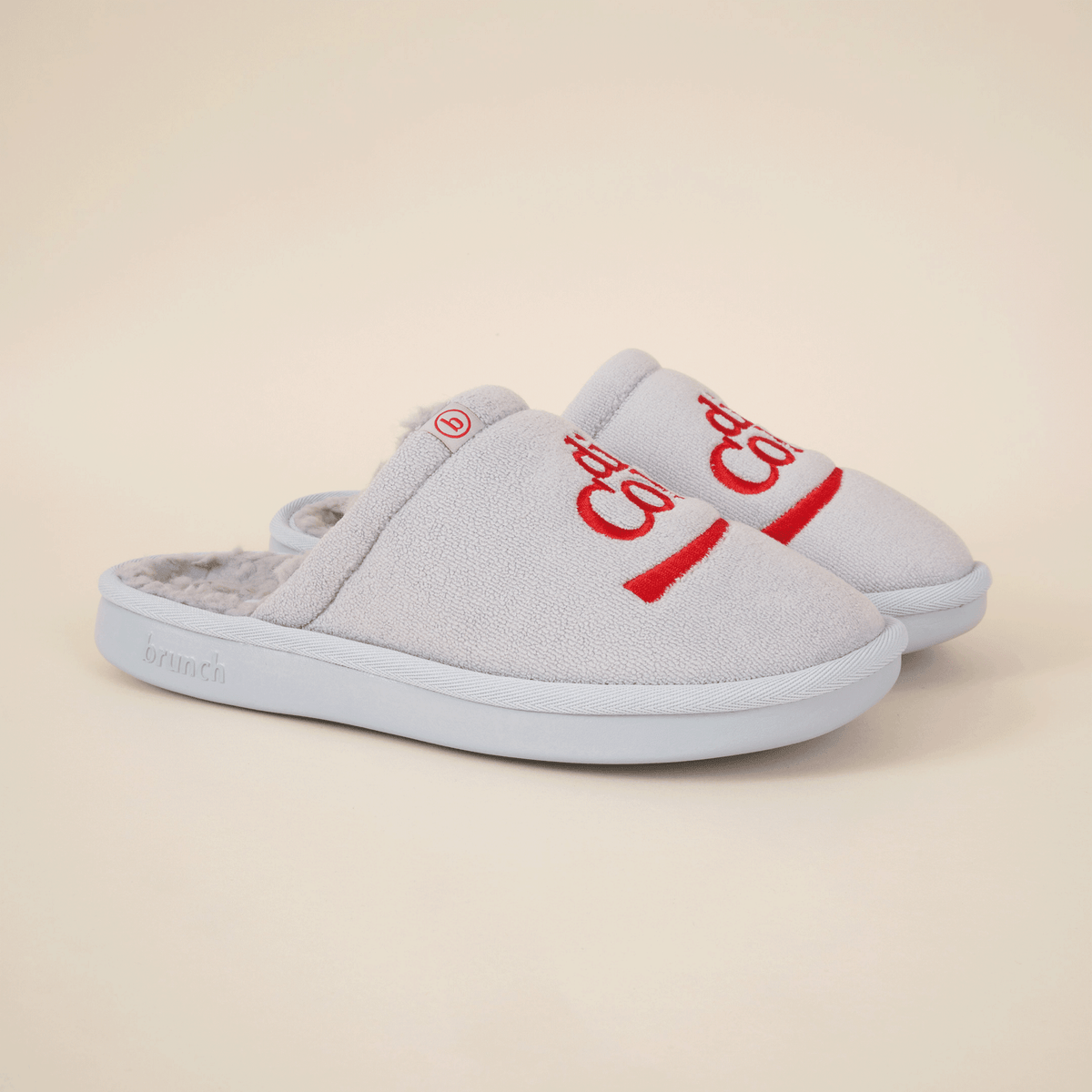 Angled view of grey Diet Coke collab slippers with red embroidered logo, faux shearling lining and molded sole