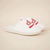 Angled view of white Brunch x Diet Coke slippers with red embroidered Diet Coke logo and quilted upper on beige background