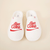 Overhead view of white L'Essentiel slippers showcasing red embroidered diet Coke logo and quilted upper on beige background