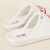 Three-quarter view of white Diet Coke x Brunch quilted slippers with red embroidered logo, terry footbed labels, and cushioned platform on a beige background