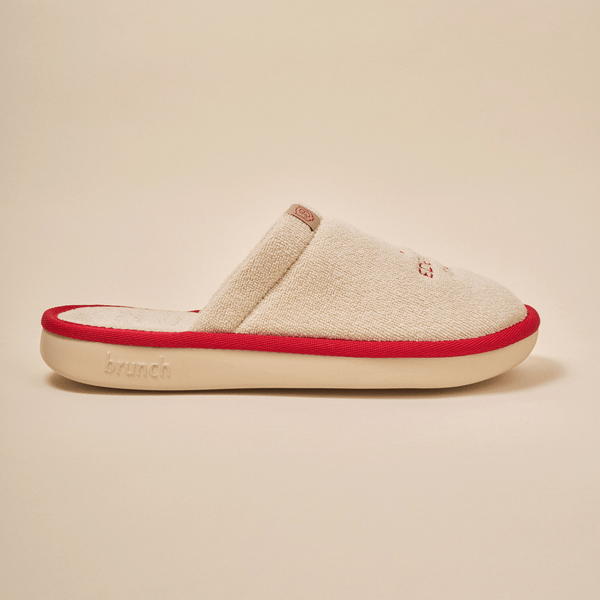 Side view of Essential Eden Rock slipper in beige with soft terry upper, red trim and Eden Roc embroidery on neutral backdrop