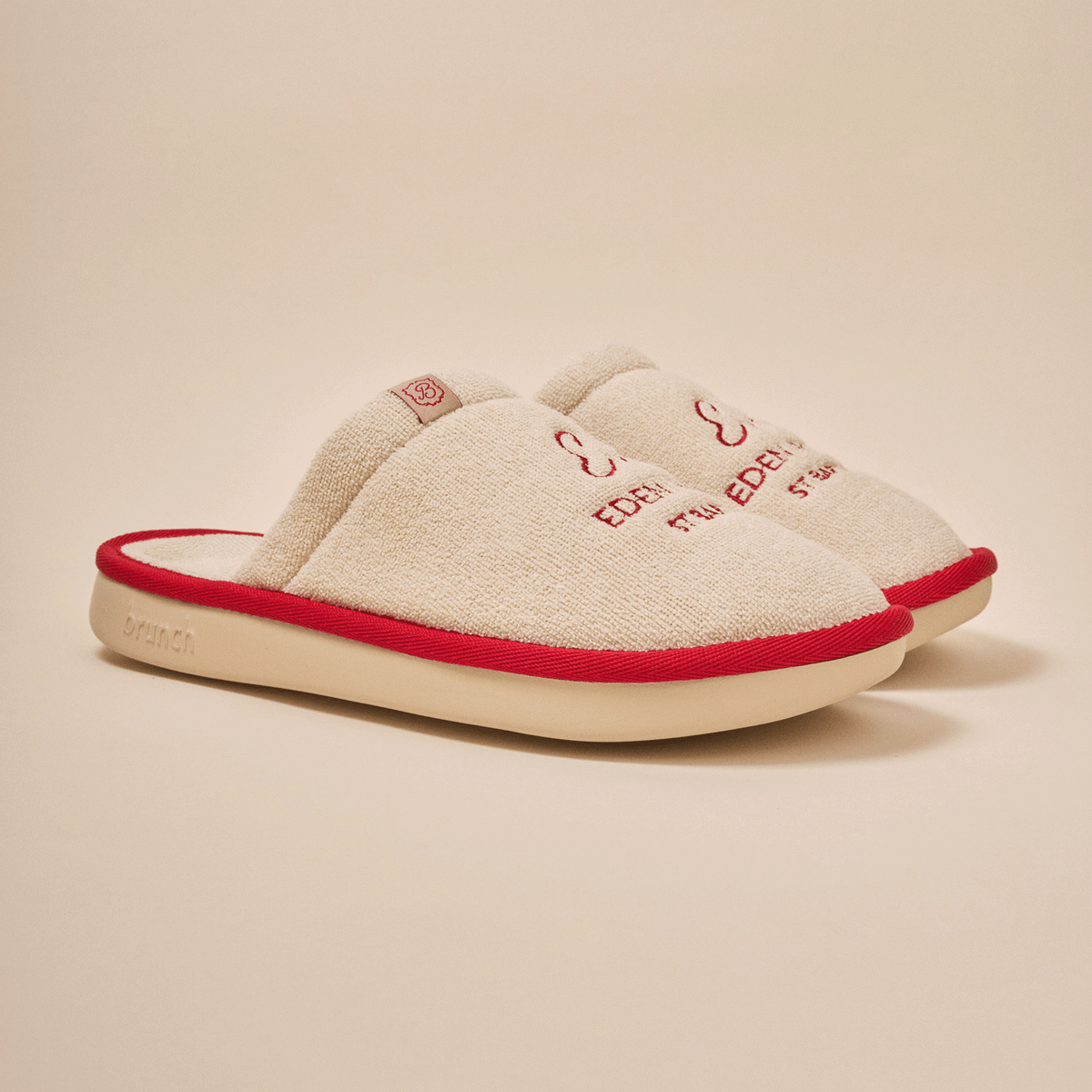 Three-quarter view of beige Essential Eden Rock slipper with terry upper, red Eden Roc embroidery, red trim and cream EVA sole