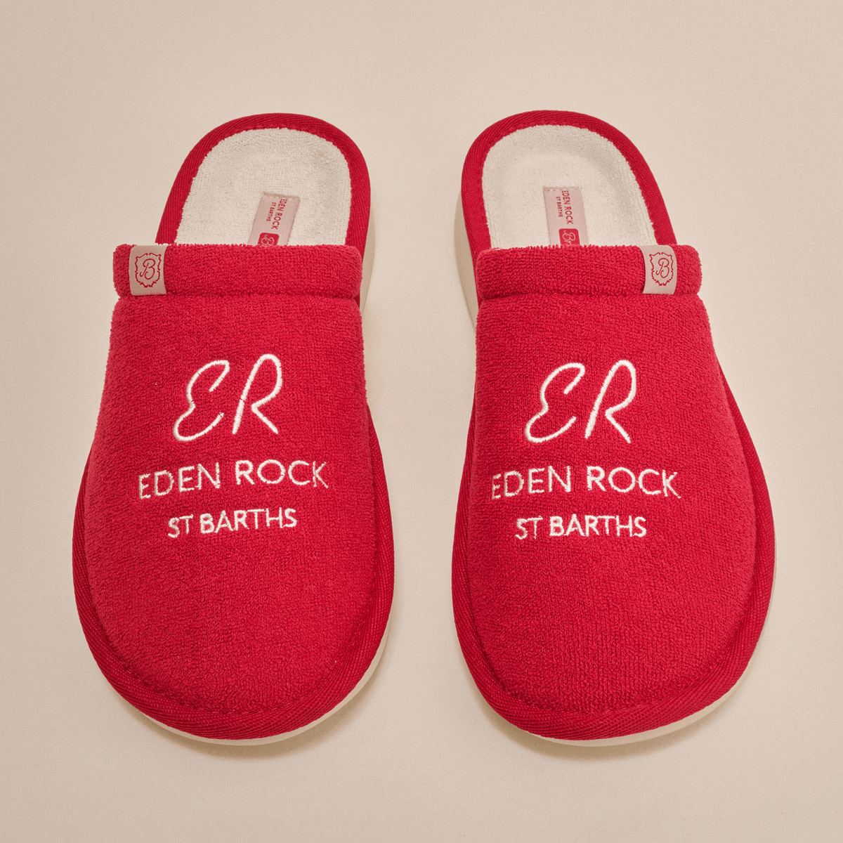 Top-down view of Essential Eden Rock red slip-on slippers showcasing white embroidered text ER EDEN ROCK ST BARTHS on terry uppers with cream background