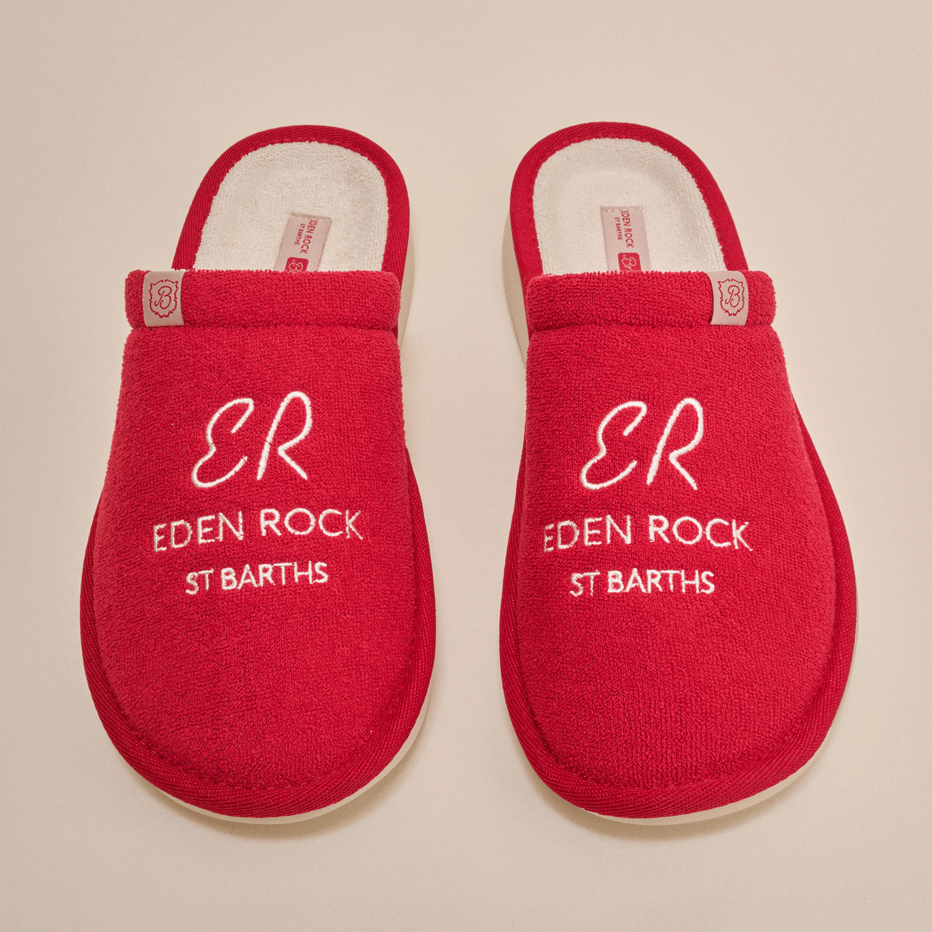 Top-down view of Essential Eden Rock red slip-on slippers showcasing white embroidered text ER EDEN ROCK ST BARTHS on terry uppers with cream background