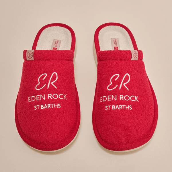 Top-down view of Essential Eden Rock red slip-on slippers showcasing white embroidered text ER EDEN ROCK ST BARTHS on terry uppers with cream background