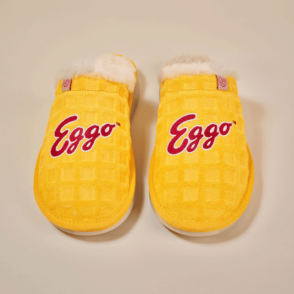 Top-down view of Essential Eggo slippers showing yellow waffle-textured suede, red "Eggo" embroidery, and white shearling lining