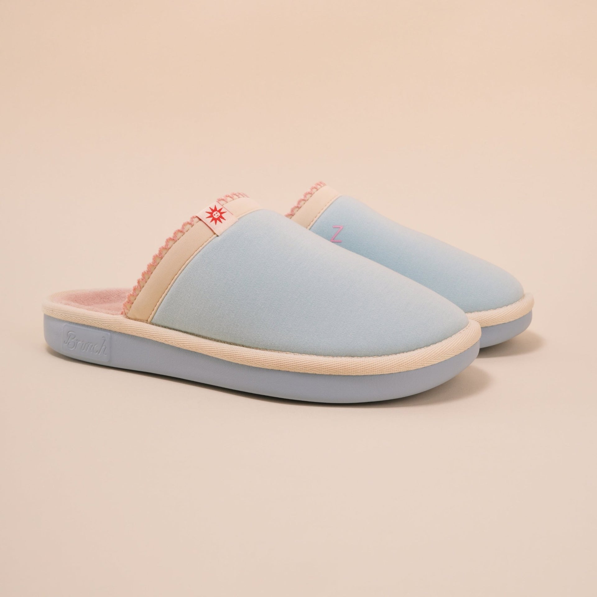 Angled view of Essential Cozyland slipper showing light blue upper, pink plush terry lining and cushioned sole on beige background