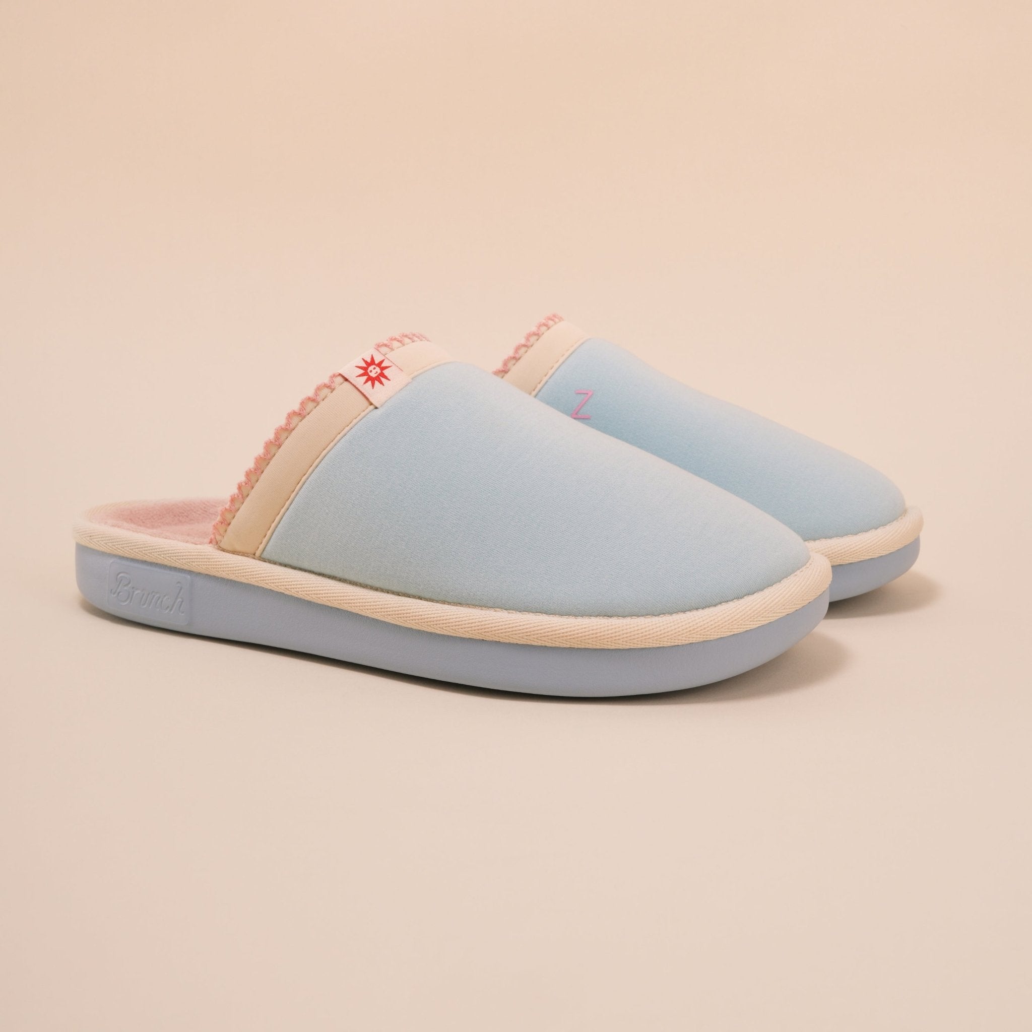 Angled view of Essential Cozyland slipper showing light blue upper, pink plush terry lining and cushioned sole on beige background