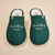 Top-down view of green Essential slippers embroidered with The Beverly Hills Hotel and Bungalows text on a beige background