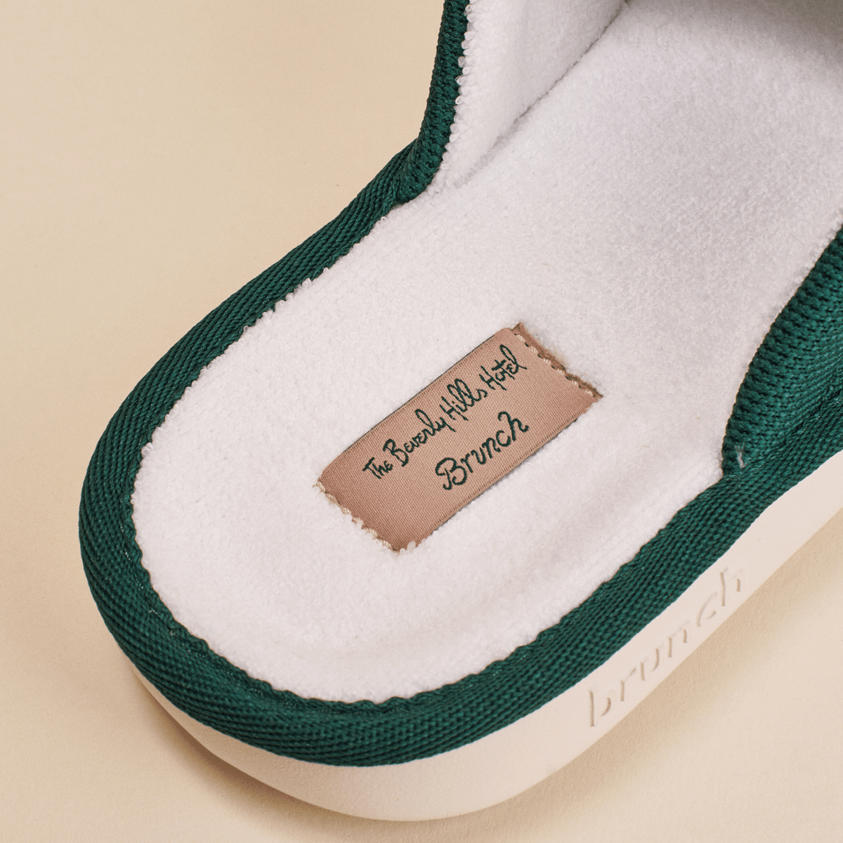 Close-up of Essential Beverly Hills Hotel slipper insole showing white terry lining, pink label reading The Beverly Hills Hotel Brunch and green knit trim