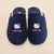 Top-down view of navy terry Hello Kitty slippers with embroidered faces and pink Hello Kitty script on beige background