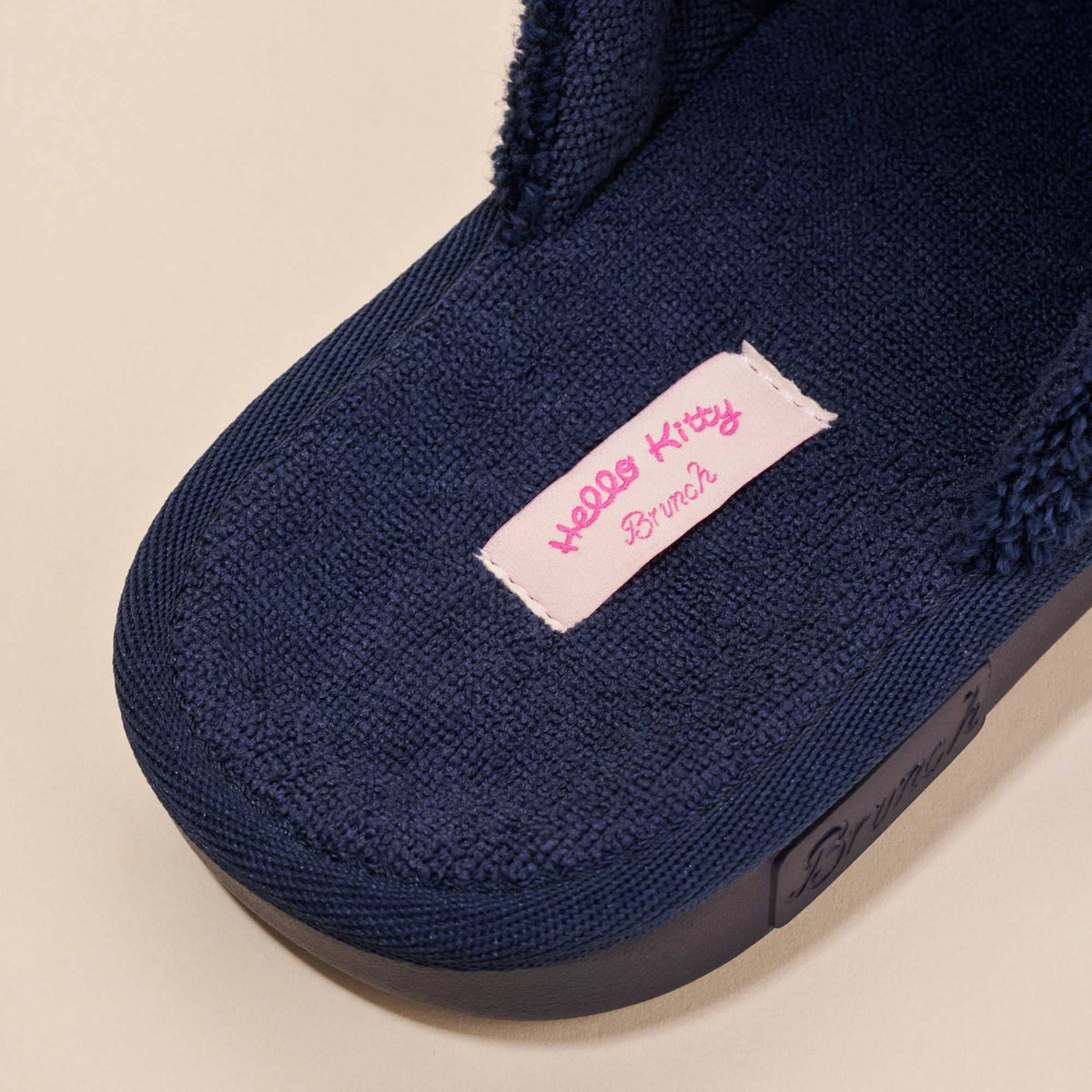 Close up of Hello Kitty navy terry slipper footbed showing textured terry fabric and molded EVA sole on beige background
