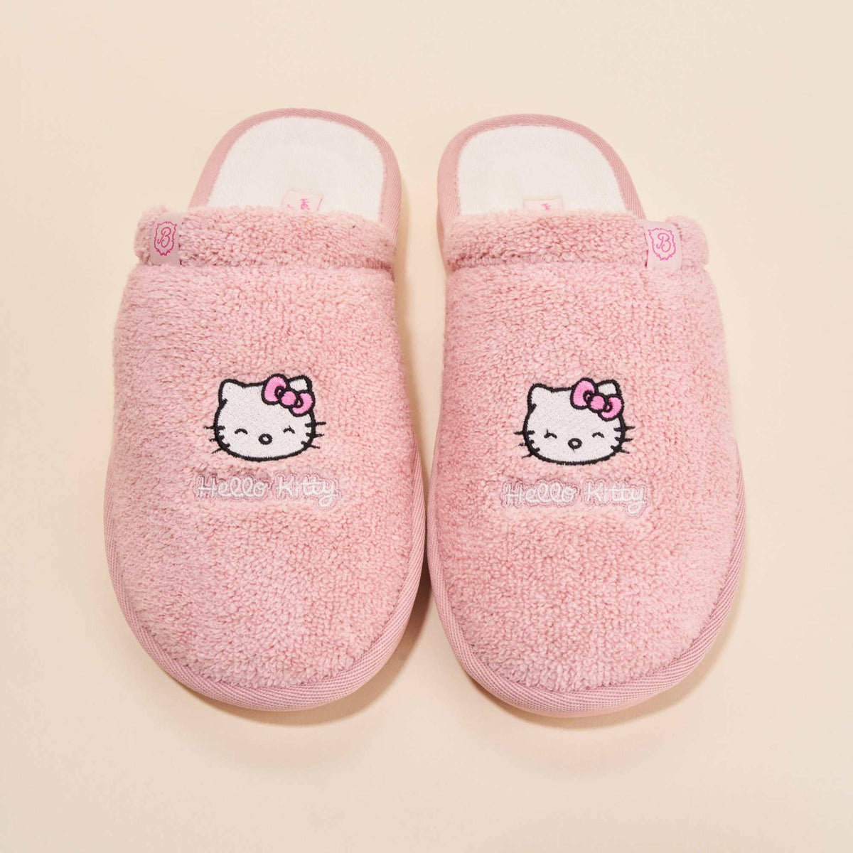 Top view of Essential Hello Kitty terry slippers showcasing embroidered Hello Kitty faces on pink terry fabric with cream background