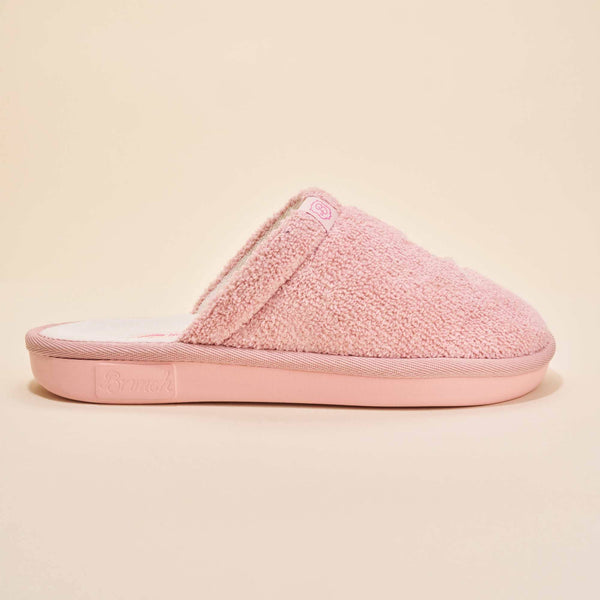Side view of pink Hello Kitty terry slipper showing plush terry upper, embroidered Hello Kitty tag, and molded Brunch sole on a beige background