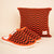 Three-quarter view of Amber Hirshleifers knit slippers showing orange and black checker knit upper and white foam sole on beige background