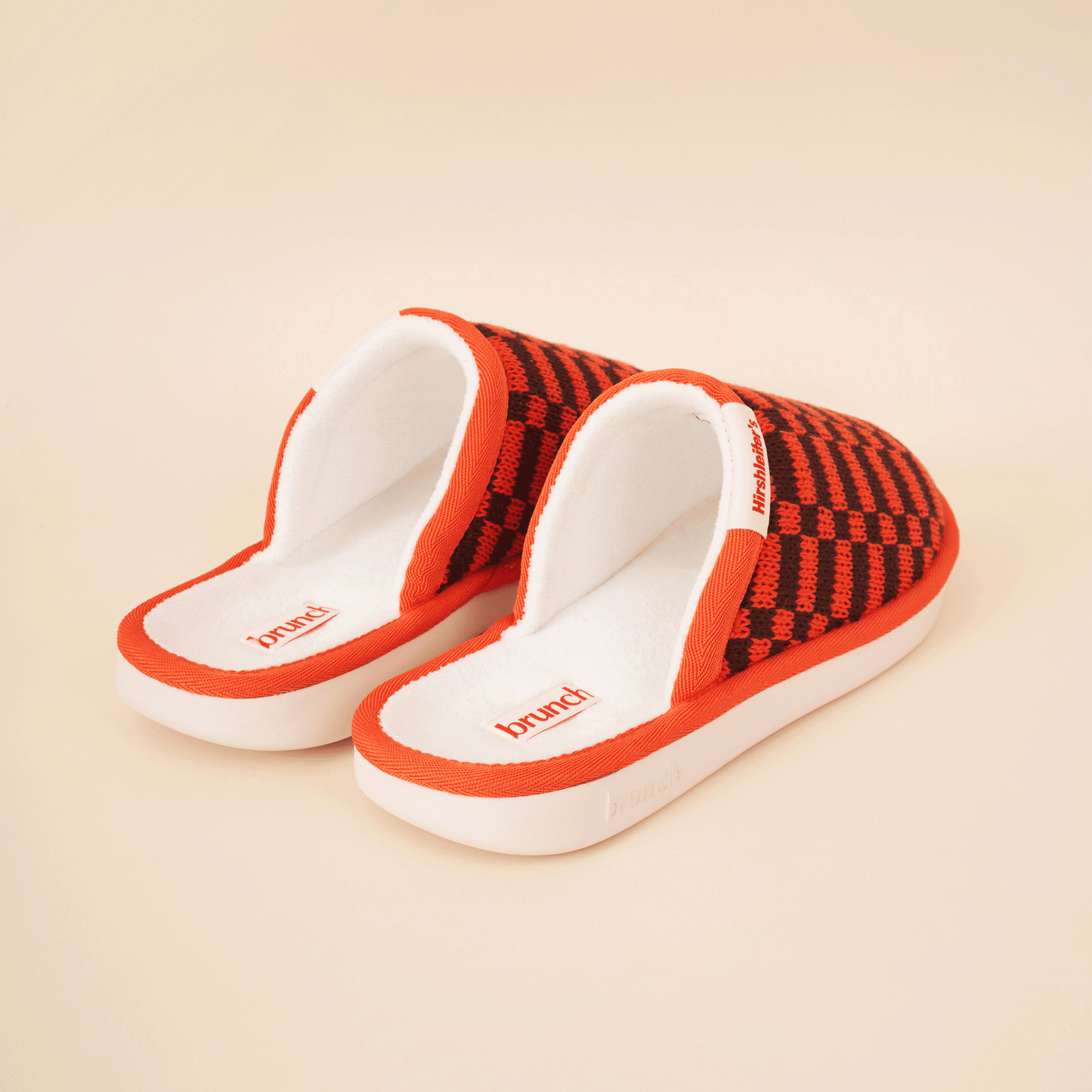 Three-quarter view of Amber Hirshleifers slipper with orange-black knit upper and white cushioned footbed on cream background
