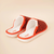 Three-quarter view of Amber Hirshleifers slipper with orange-black knit upper and white cushioned footbed on cream background