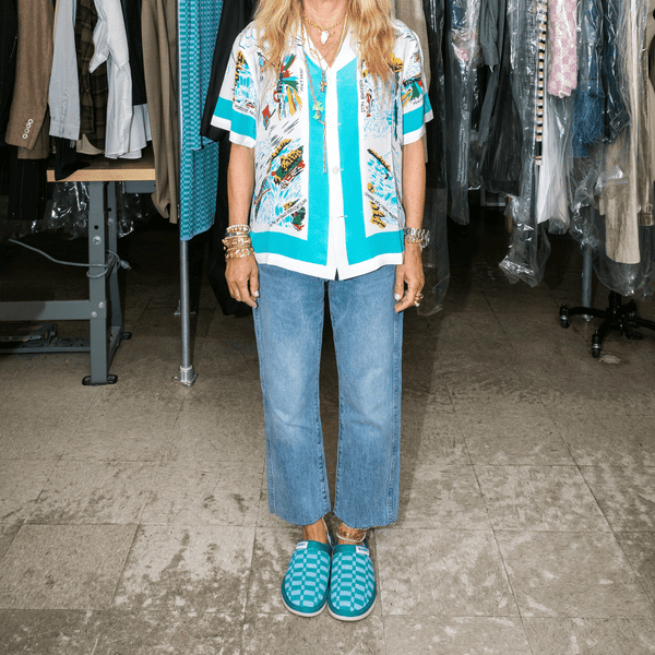 Person standing wearing marine checkered Brunch x Hirshleifers slip-on slippers with cropped jeans in a studio wardrobe setting