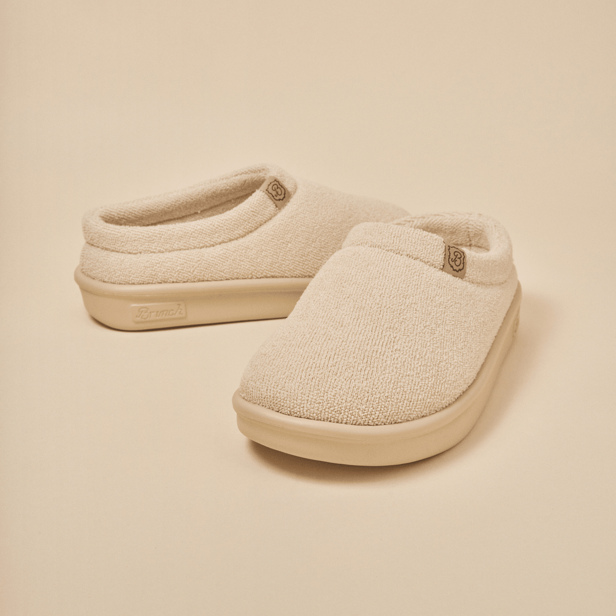 Front three-quarter view of Essential Kids slipper in beige terry showcasing terry knit upper and molded EVA outsole on a neutral background