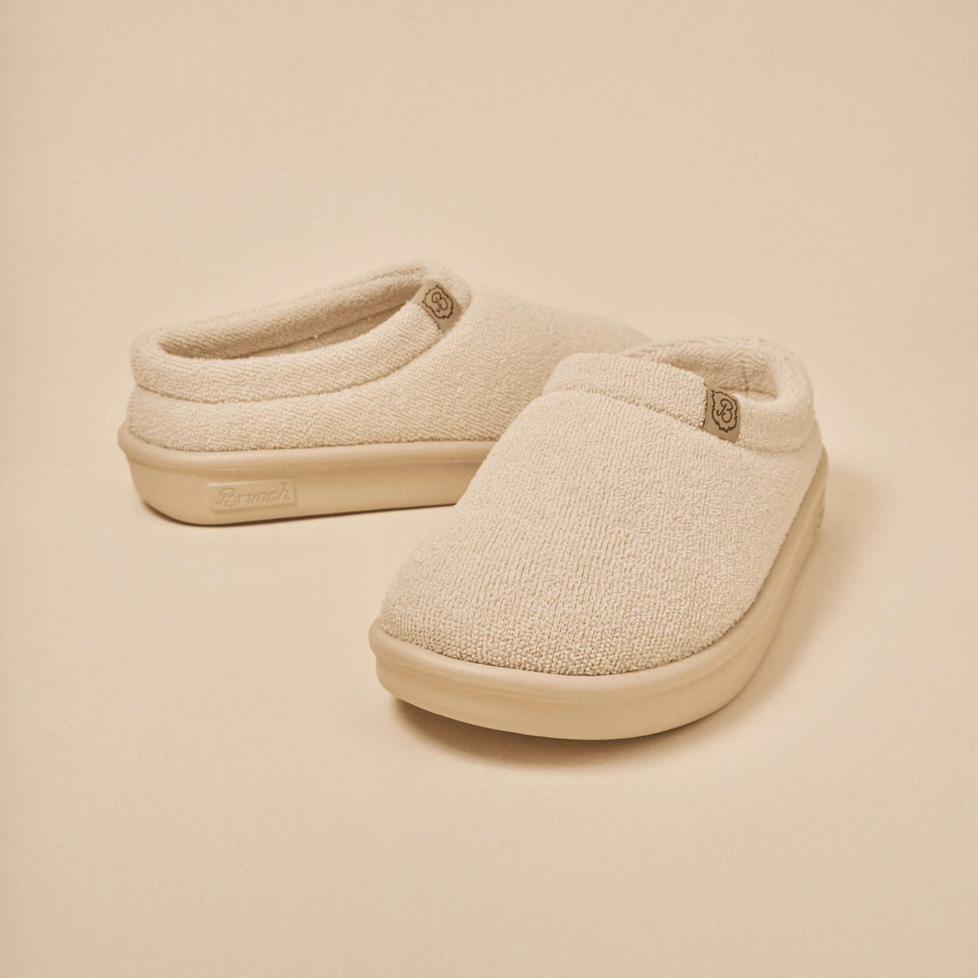 Front three-quarter view of Essential Kids slipper in beige terry showcasing terry knit upper and molded EVA outsole on a neutral background
