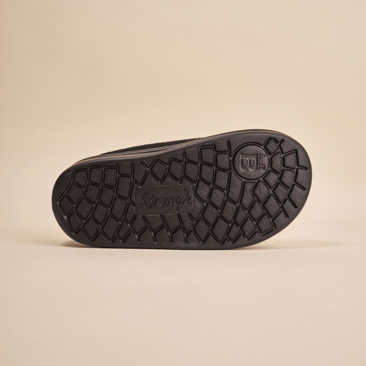 Bottom view of Essential Kids black terry slipper showing textured EVA outsole with Brunch logo on beige background