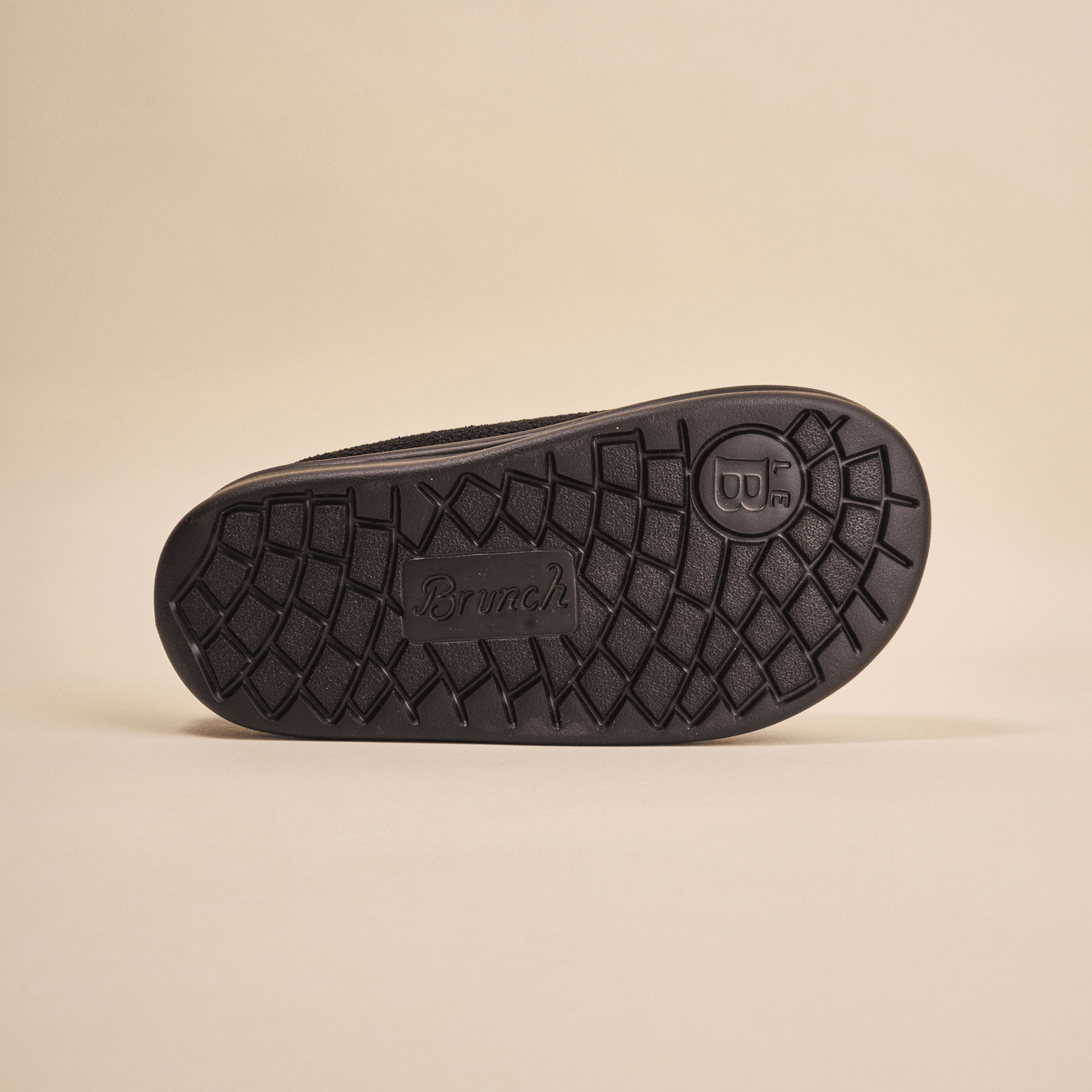 Bottom view of Essential Kids black terry slipper showing textured EVA outsole with Brunch logo on beige background