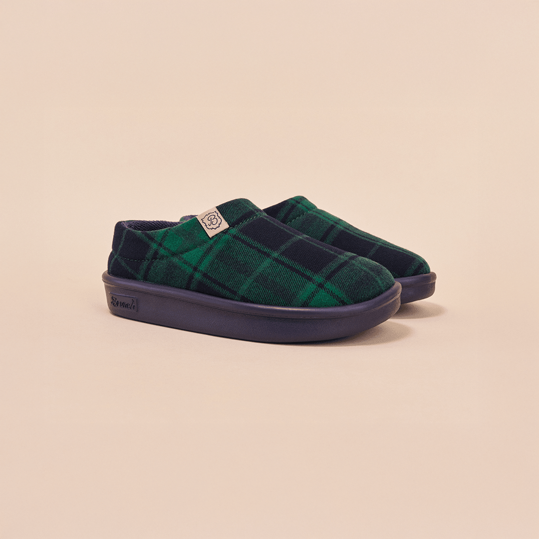 Angled side view of Essential Kids slipper showcasing navy and green plaid recycled polyester upper and navy EVA outsole on pale beige background