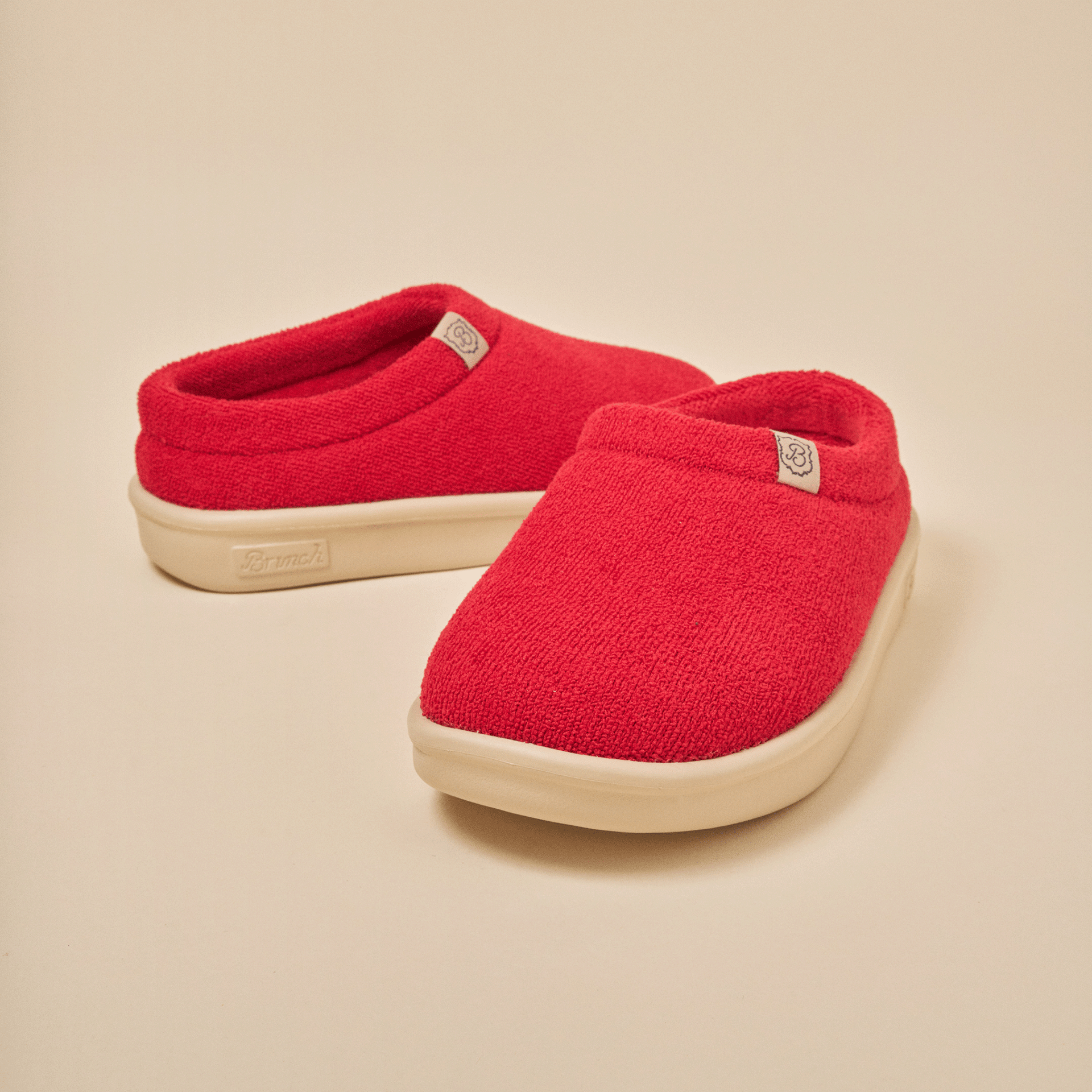Front three-quarter view of Essential Kids red terry slip-on slipper showing textured terry upper and cream EVA outsole on beige background