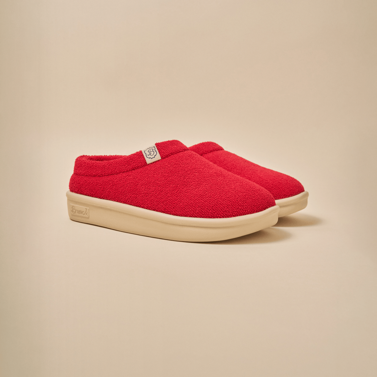 Three-quarter view of Essential Kids slipper in red terry showing plush upper and cream EVA outsole on beige background