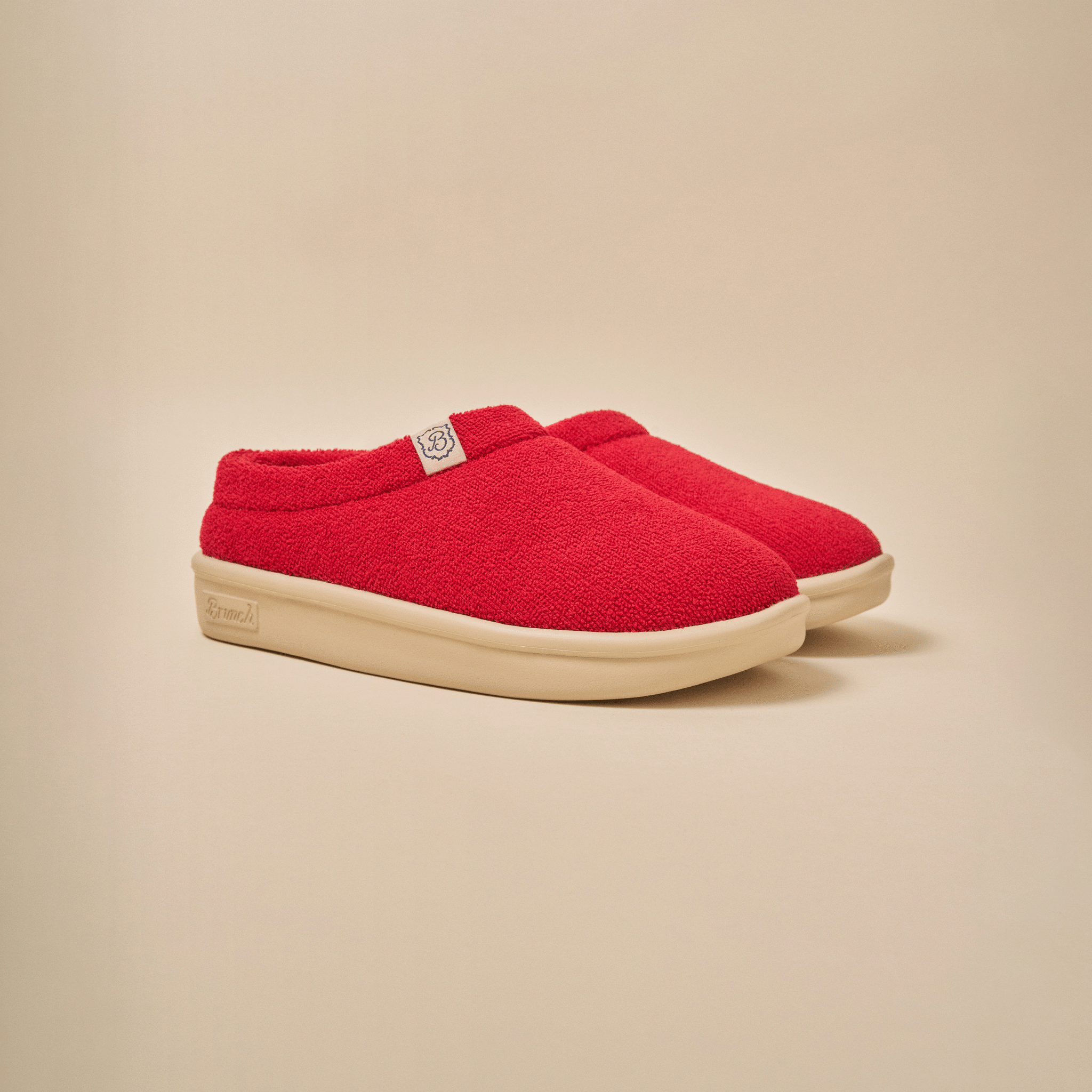 Three-quarter view of Essential Kids slipper in red terry showing plush upper and cream EVA outsole on beige background