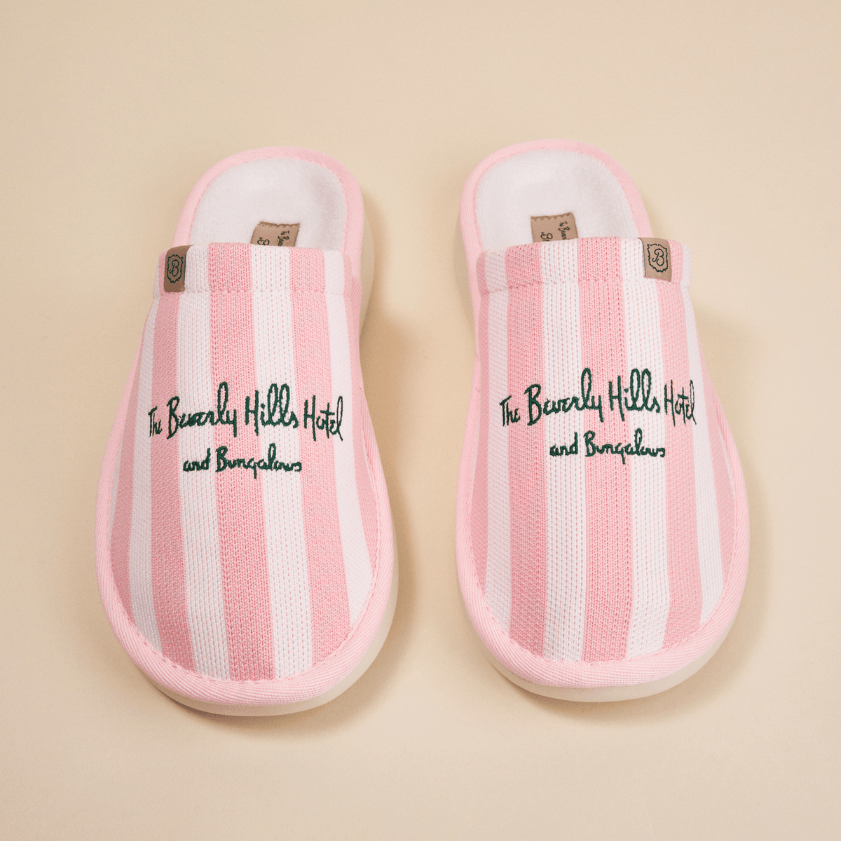 Overhead view of pink striped Essential slippers with embroidered Beverly Hills Hotel text and plush lining on beige background