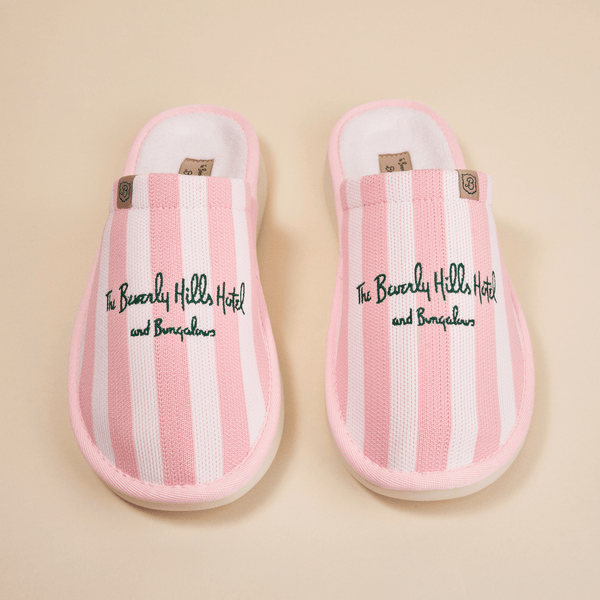 Overhead view of pink striped Essential slippers with embroidered Beverly Hills Hotel text and plush lining on beige background