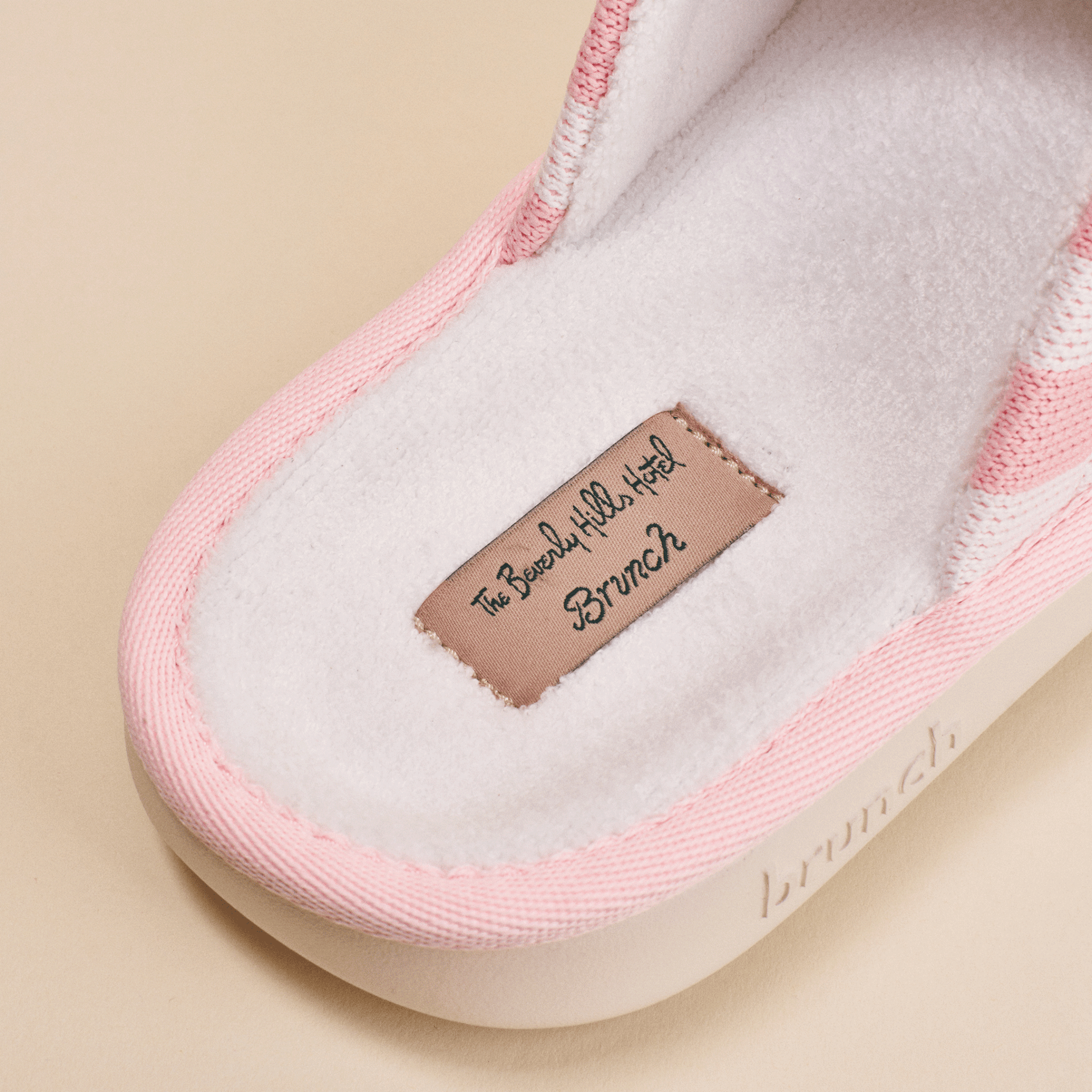 Close-up of pink Essential slipper showcasing fleece footbed and sewn label The Beverly Hills Hotel Brunch on beige background