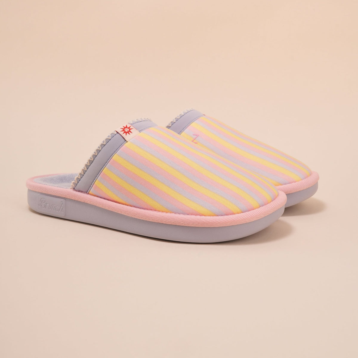 Three-quarter view of Cozyland Essential slip-on slipper with pastel rainbow stripes, pink trim and plush lining