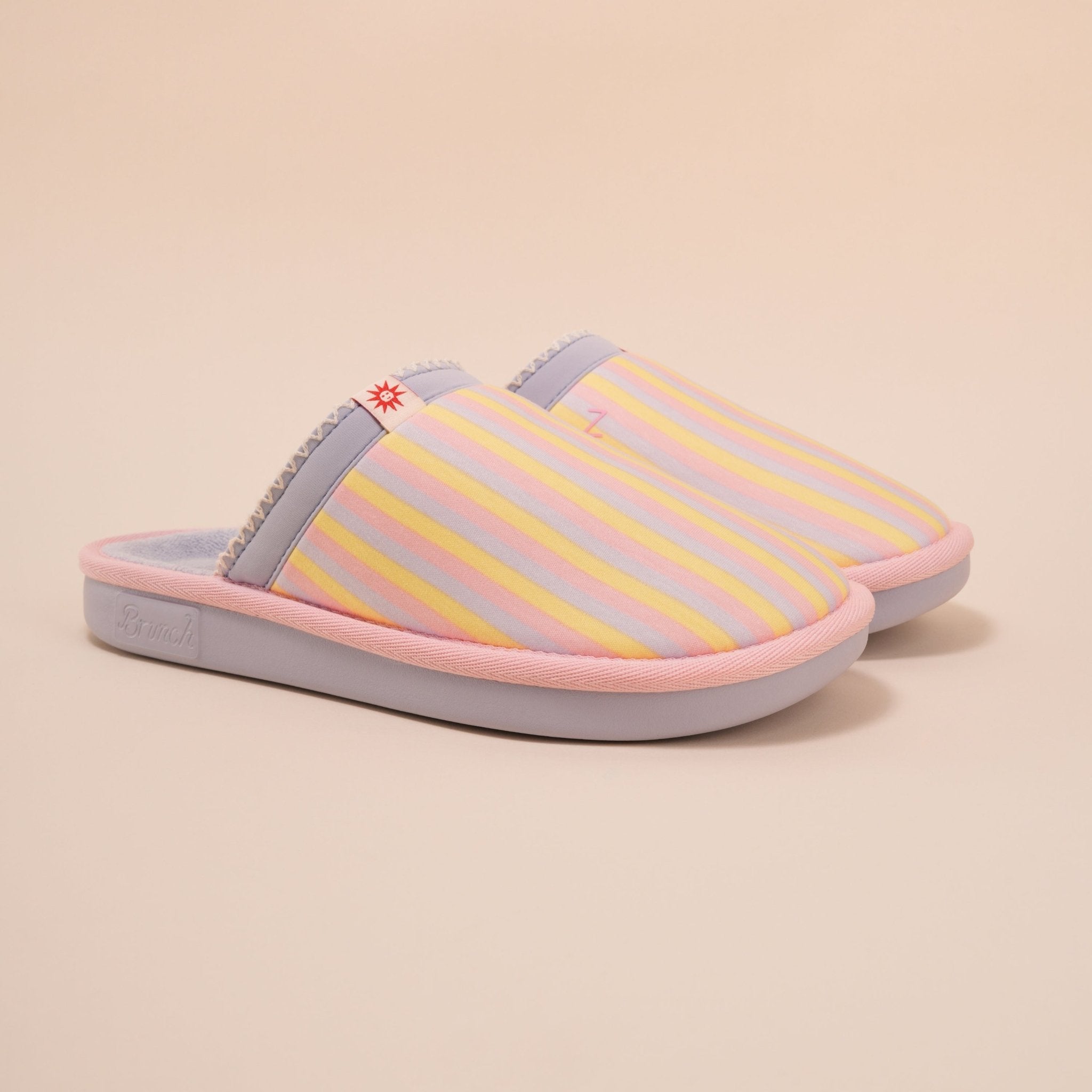 Three-quarter view of Cozyland Essential slip-on slipper with pastel rainbow stripes, pink trim and plush lining