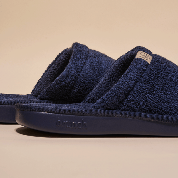 Close-up side view of navy Essential Slipper showing terry-cloth open-toe upper and embossed Brunch sole on beige background