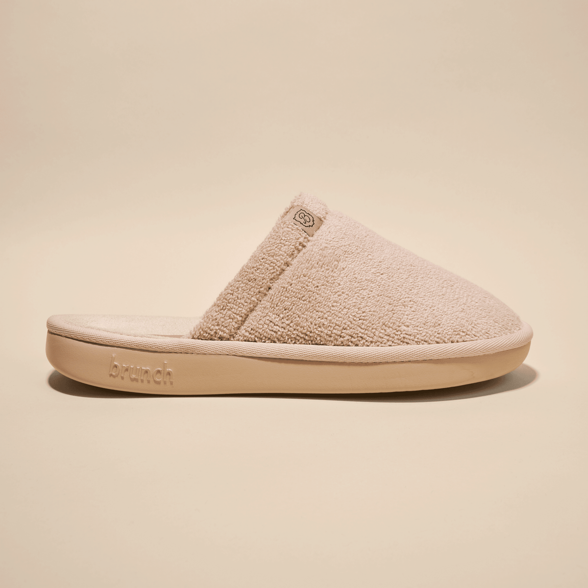 Side view of beige Essential slipper showing plush terry upper and low-profile open-back silhouette on studio background
