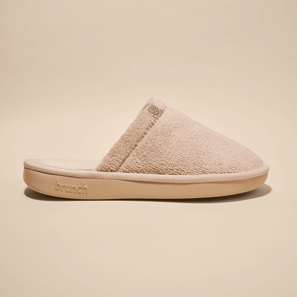 Side view of beige Essential slipper showing plush terry upper and low-profile open-back silhouette on studio background