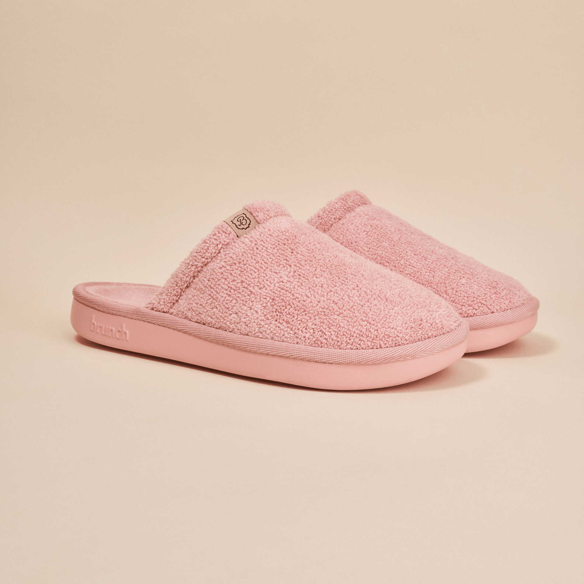 Three-quarter view of pink Essential Slipper showing plush terry upper, open-back slip-on style and cushioned molded sole on neutral background