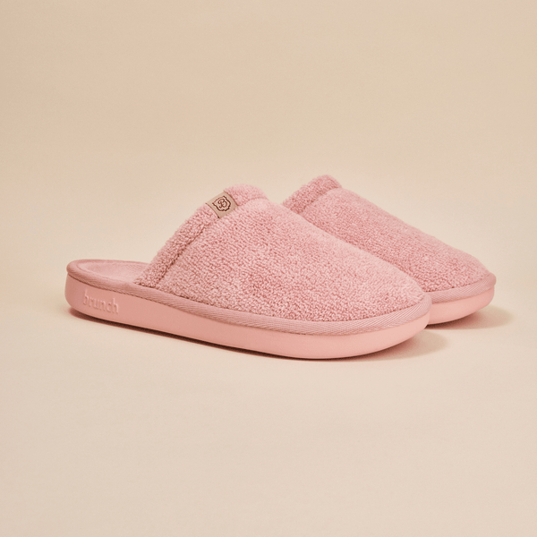 Three-quarter view of pink Essential Slipper showing plush terry upper, open-back slip-on style and cushioned molded sole on neutral background