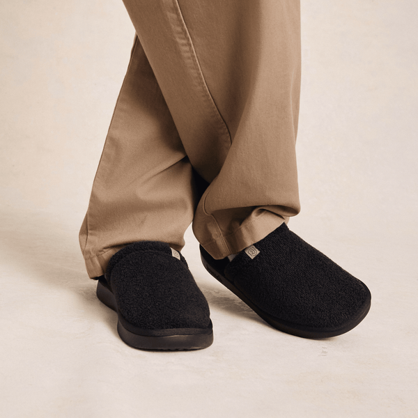 Front three-quarter view of Essential Slipper in black showing plush sherpa upper and molded sole on neutral studio background