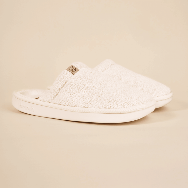 Side view of Brunch Essential slipper showcasing cream terry upper and cushioned white sole on beige background