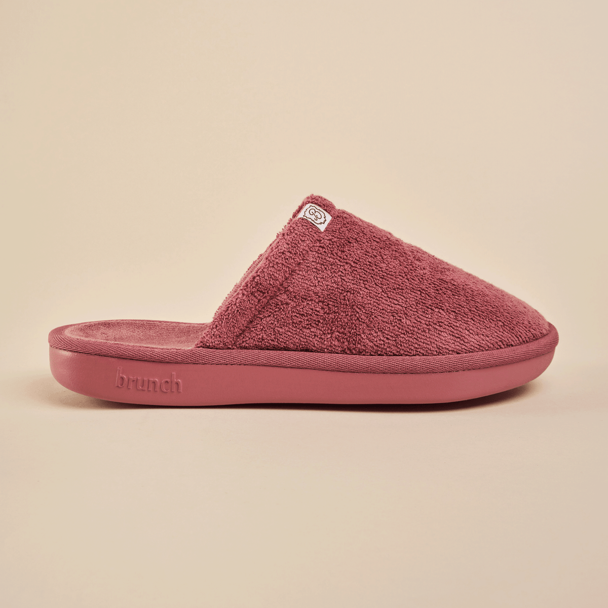Side view of Essential Slipper showing plush terry upper, molded cushioned sole and Brunch logo on a neutral beige background