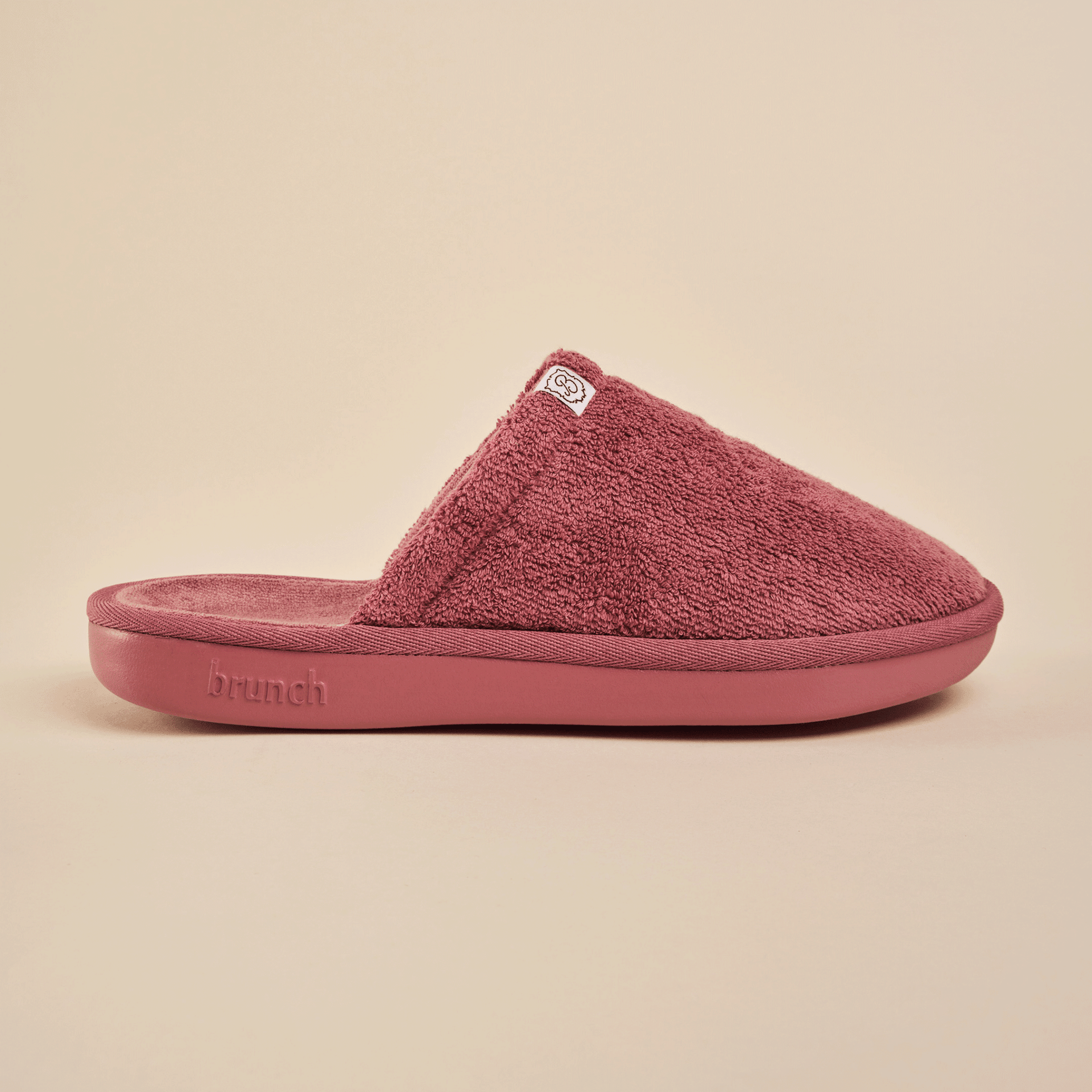 Side view of Essential Slipper showing plush terry upper, molded cushioned sole and Brunch logo on a neutral beige background