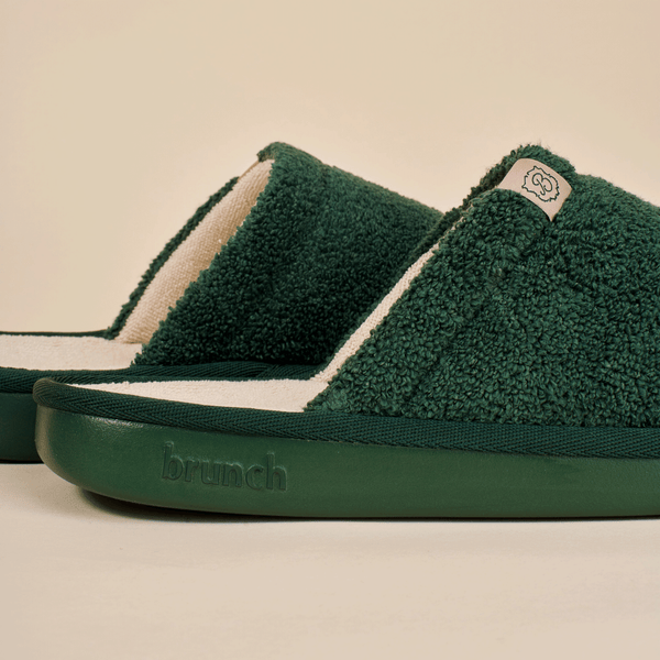 Side view of green Essential slipper with plush terry upper, cream footbed and embossed brunch sole on beige background