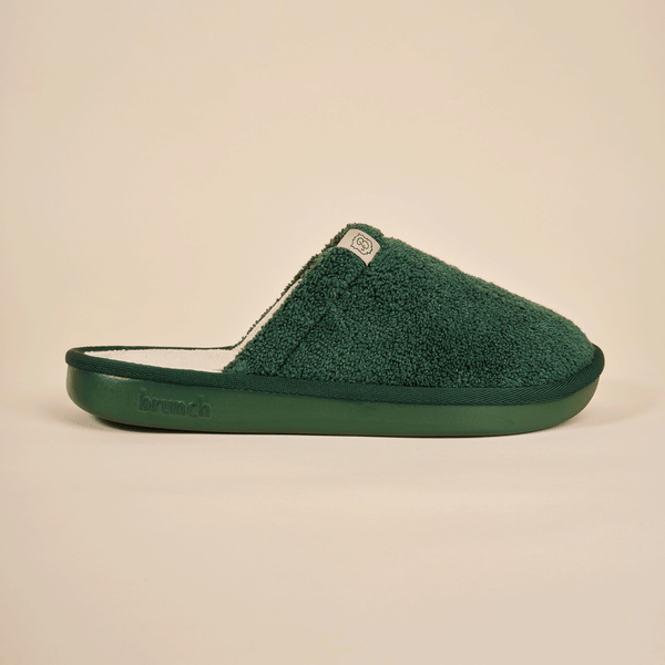 Side view of Essential Slipper showcasing forest green terry upper and cushioned branded sole on beige background