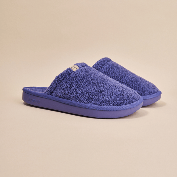 Three-quarter view of Essential slipper showcasing blue terry-cloth upper and cushioned rubber sole on beige background