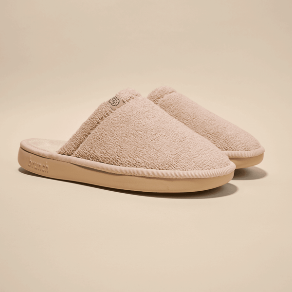 Three-quarter view of Essential Slipper showcasing beige terry-cloth upper and cushioned tan sole on a neutral background