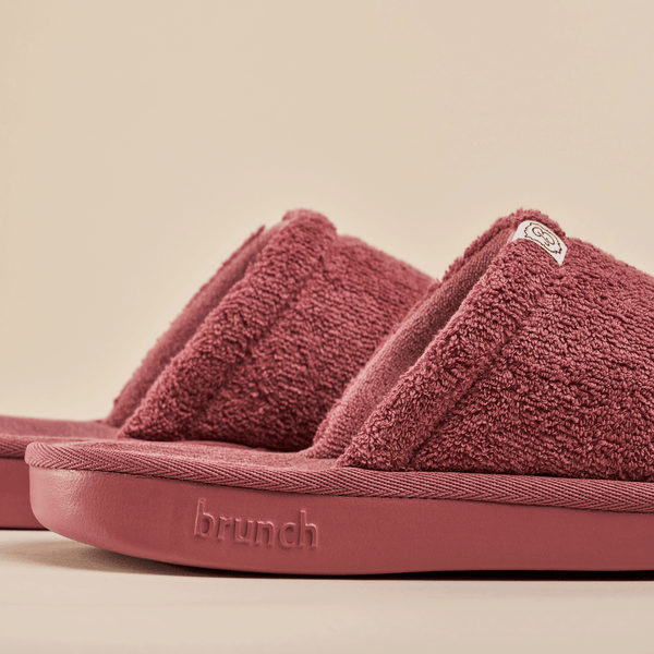 Close-up of Essential slipper in rose showing terry-cloth upper, open-toe design and embossed brunch logo on beige background